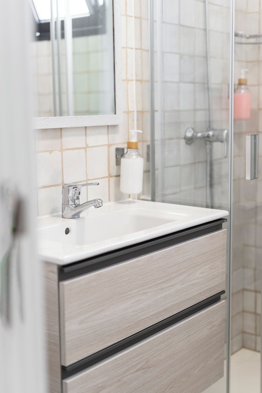 A modern bathroom with a glass shower enclosure, a white sink with a chrome faucet, and a mirror above the sink.