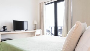 A hotel room with a bed, a desk with a television, a lamp, and a view of the outside balcony. - Casa das Proteas (Santana)