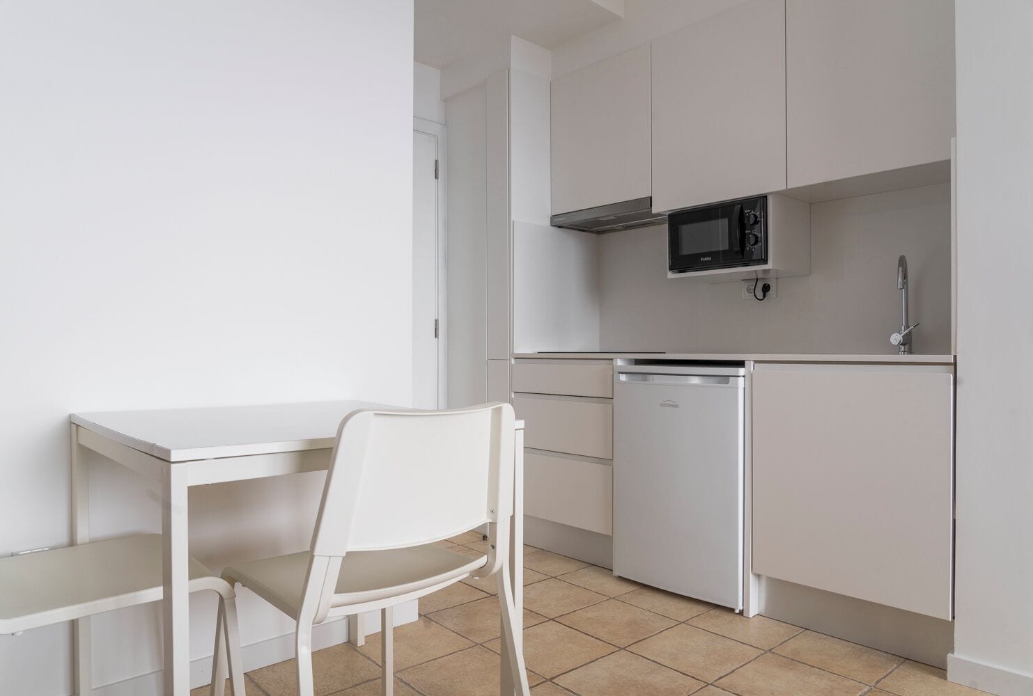 A compact kitchen with white cabinetry, a microwave, a dishwasher, and a small dining table with a chair.