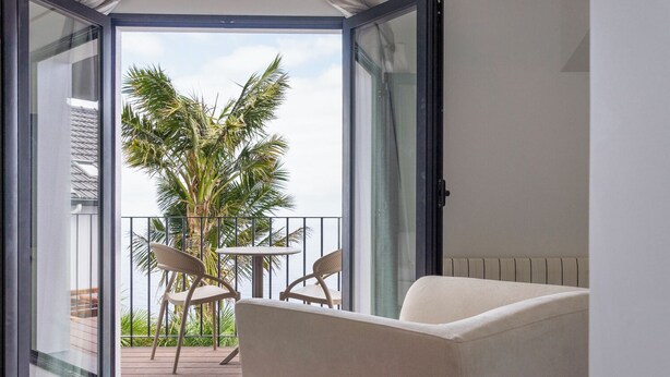A balcony with a view of palm trees, a table, and two chairs. - Casa das Proteas (Santana)