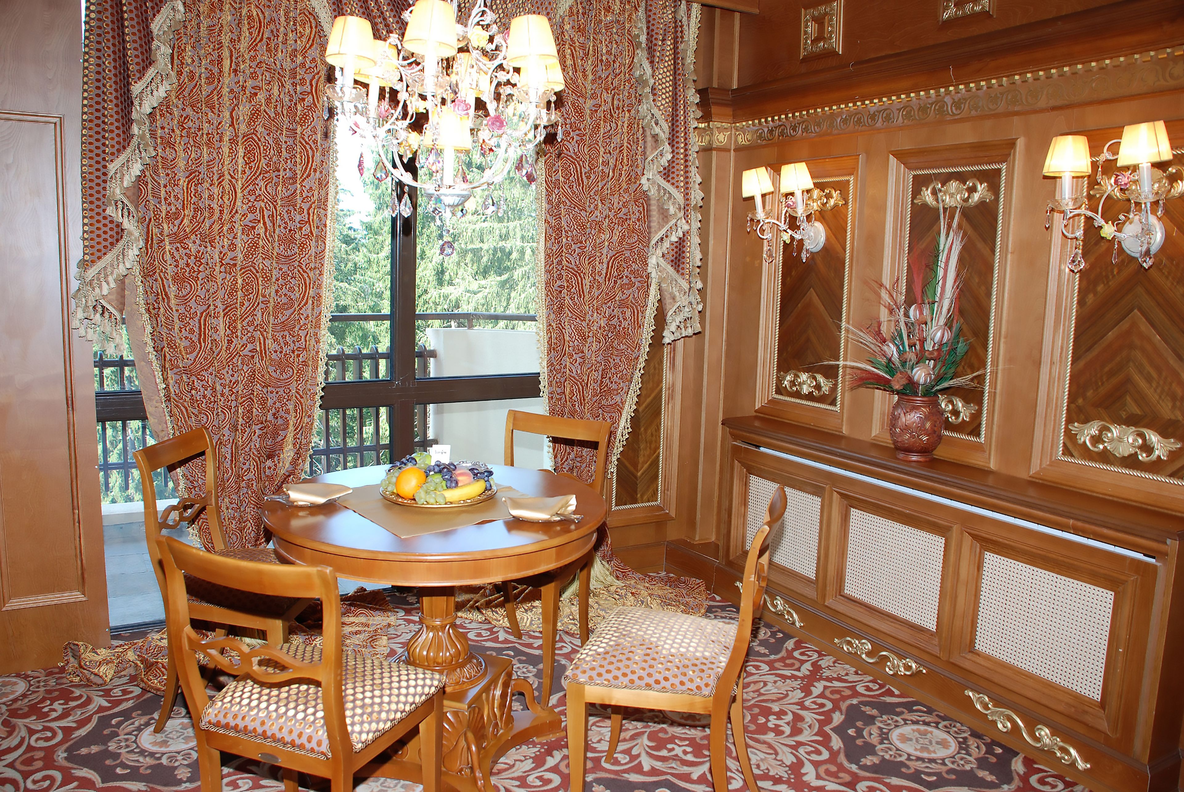 A dining area with a round table, chairs, a chandelier, and a window with curtains.