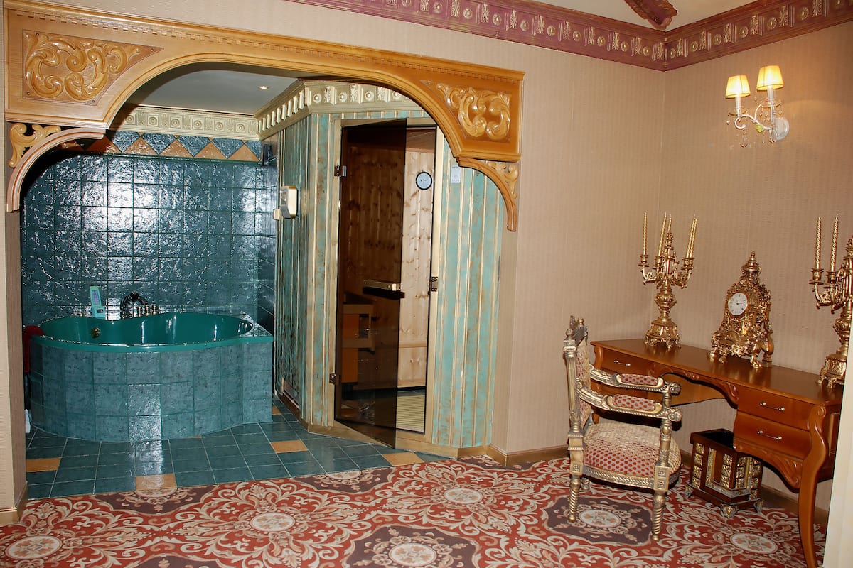 A bathroom with a large bathtub, a wooden vanity with a mirror, and a patterned floor.