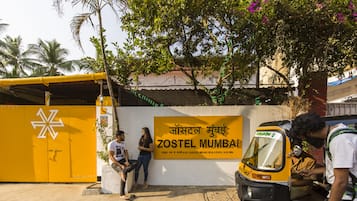 Un edificio amarillo con un cartel que dice "ZOSTEL MUMBAI" y un auto-rickshaw estacionado.