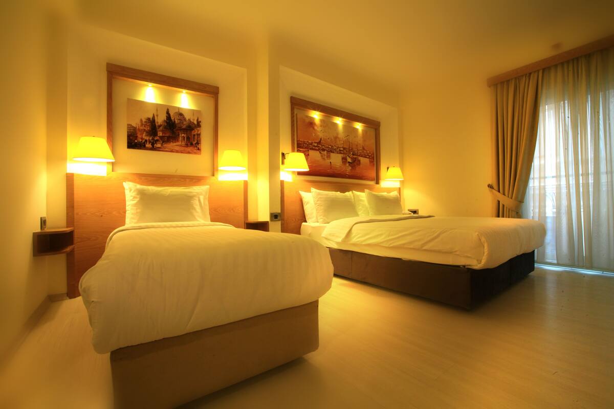 A hotel room with two beds, each with a headboard, bedside lamps, and a painting above the headboards.
