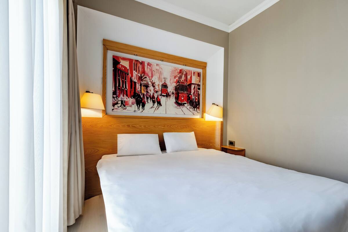 A hotel room with a large bed, two bedside lamps, and a painting on the wall.