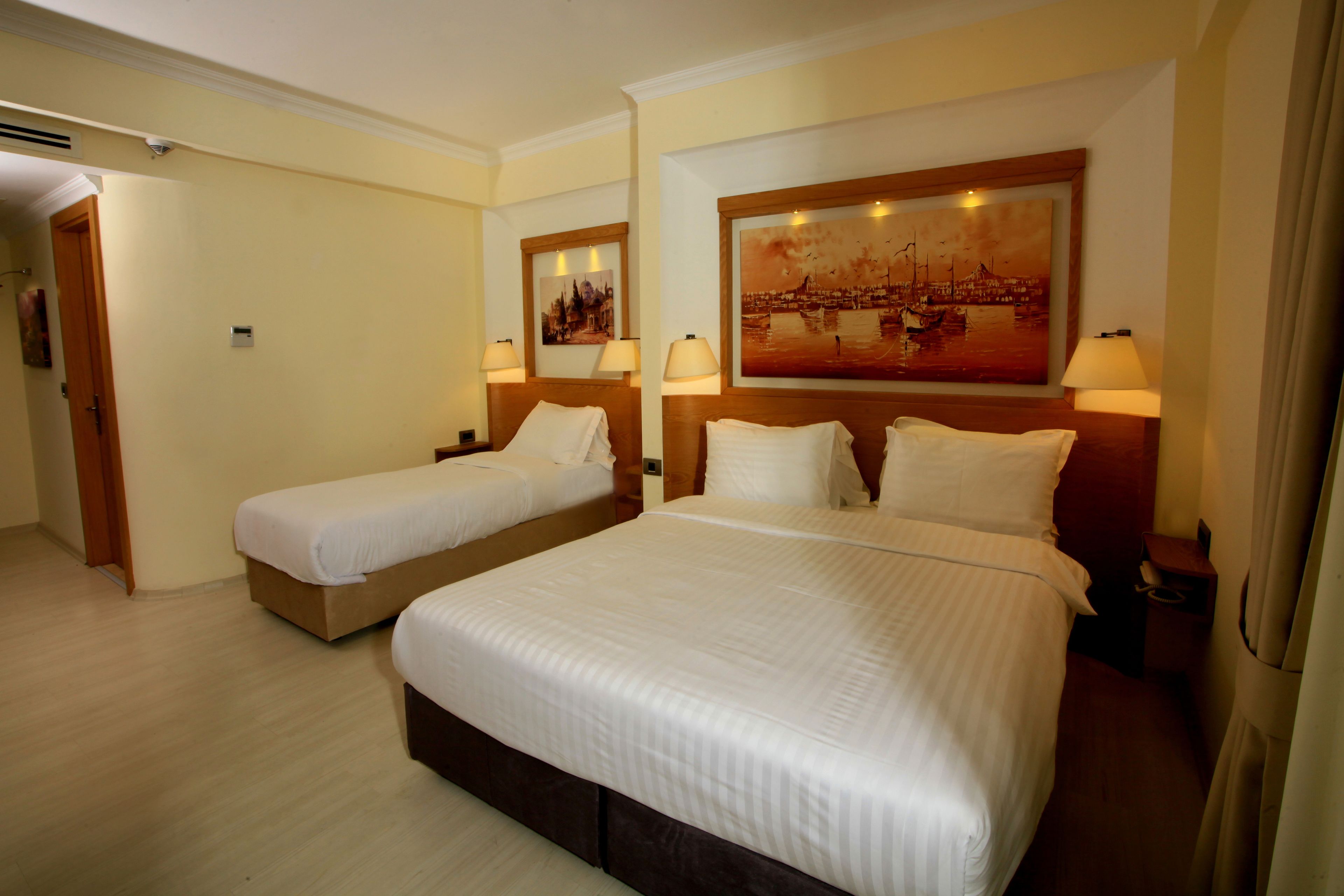 Habitación de hotel con dos camas, un cuadro grande en la pared y suelo de madera.