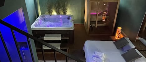 A room with a bed, a small table with a hot tub, and a staircase.