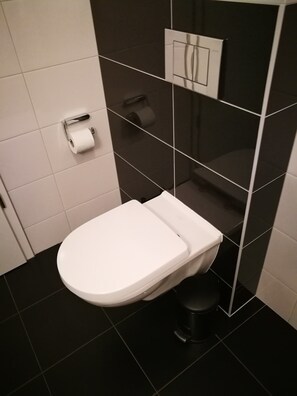 A modern bathroom with a white toilet, black tiled walls, and a visible toilet paper holder. - SHS Suite Home Sweet Strassen III (Strassen)