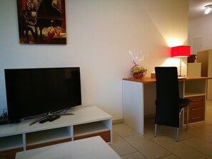 A modern living room with a flat-screen TV, a lamp, a chair, and a small table. - SHS Suite Home Sweet Strassen III (Strassen)