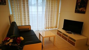 Una sala de estar con un sofá, una mesa de centro, un televisor sobre un mueble bajo y un florero con flores.