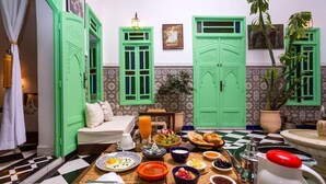 A dining area with a checkered floor, a table set with breakfast, and green doors. - Riad Rose Meryam (Marrakech)