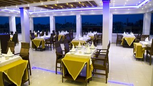 Un restaurante con mesas dispuestas para comer, ventanas amplias y vistas a la ciudad.