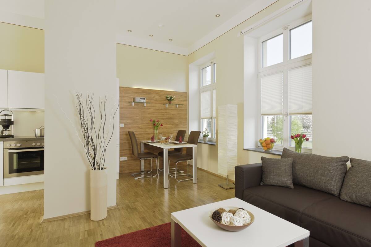 A modern living room with a brown sofa, a white coffee table, and a dining area with a wooden wall and a white table.