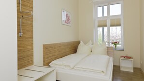 Une chambre moderne avec une tête de lit en bois, un lit recouvert de linge de lit blanc, une table de chevet et une fenêtre donnant sur un paysage verdoyant.