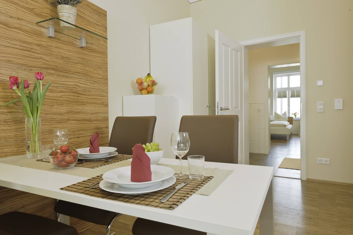 A dining area with a white table set for two, a fruit bowl, and a vase with red tulips.