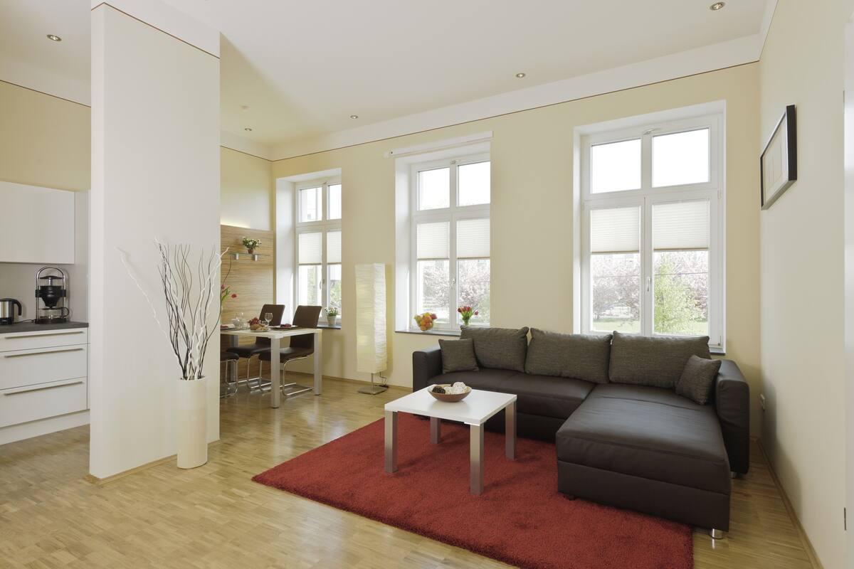 A modern living room with a sectional sofa, a dining area with a table and chairs, and a kitchen area with a coffee machine.