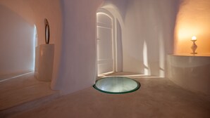A minimalist room with a glass door leading to a corridor, a white pedestal, and a small table with a candle. - Senses Suites (Santorini)
