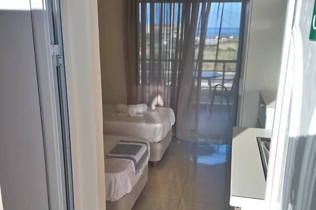 A corridor leading to a bedroom with two beds, a window with curtains, and a view of the outdoors.