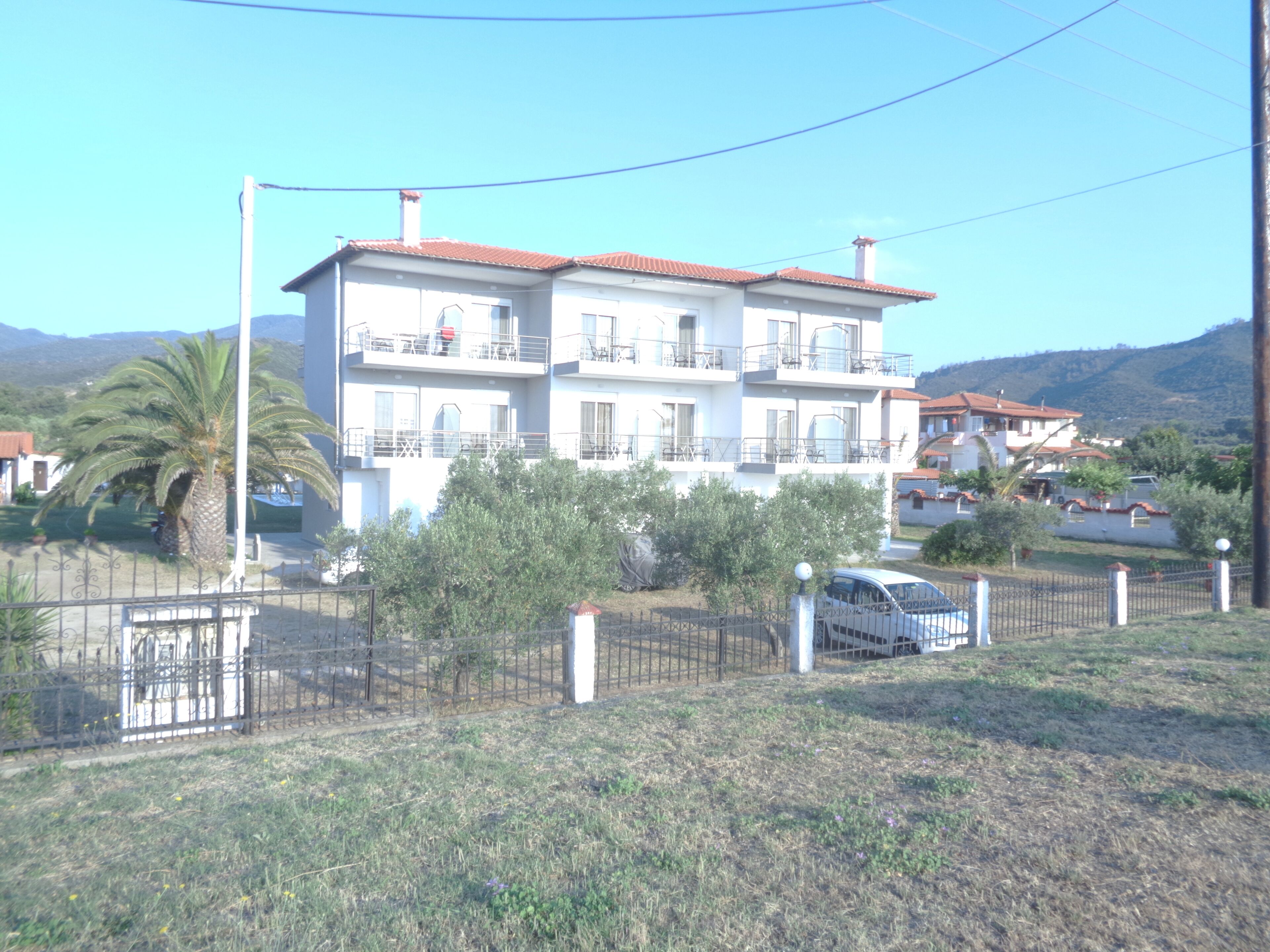 A multi-story residential building with balconies, a fenced yard, and a parked car.