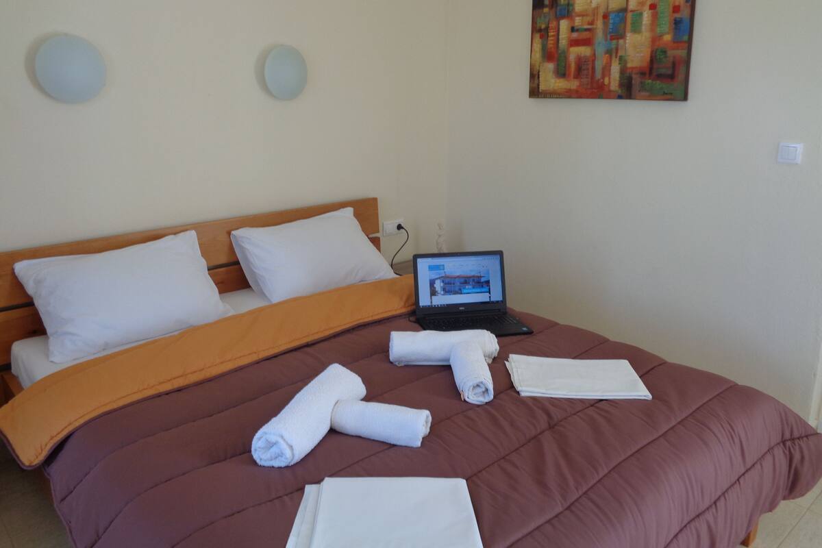 A neatly made bed with a laptop on it, a painting on the wall, and two round wall decorations.