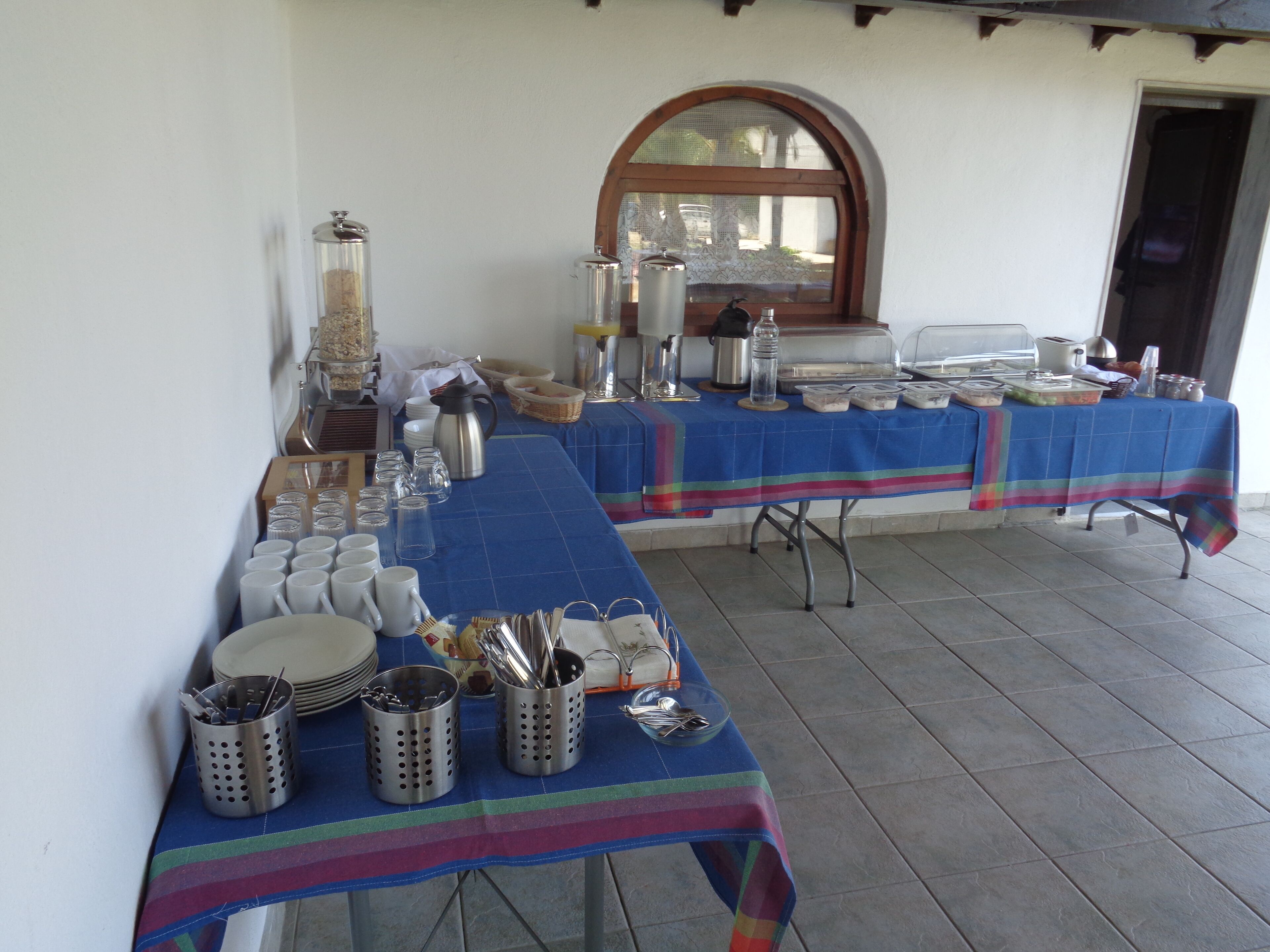A buffet table with various food items and utensils, set against a tiled floor and white walls.
