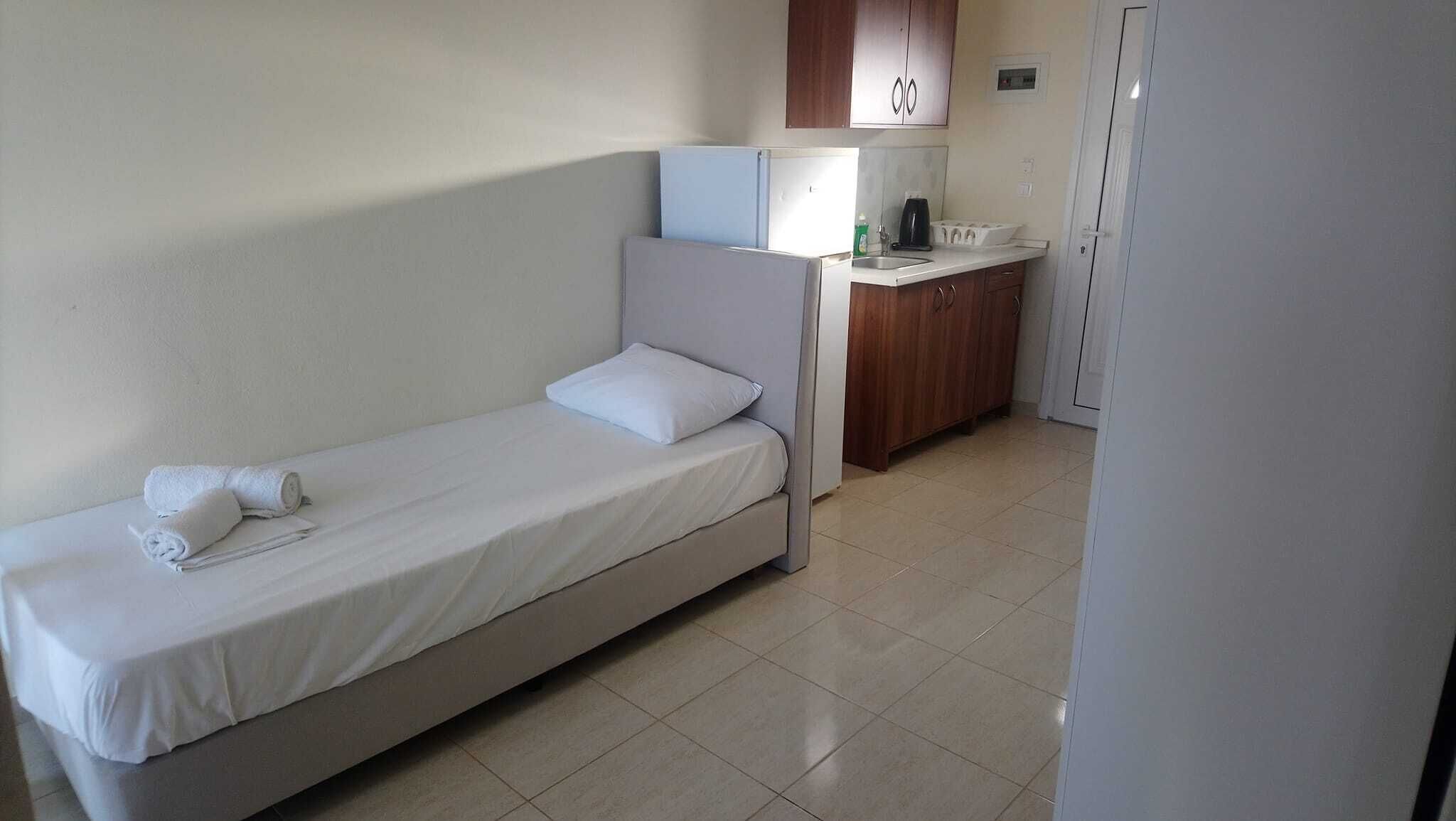 A single-bed room with a kitchenette, including a refrigerator, stove, and sink.
