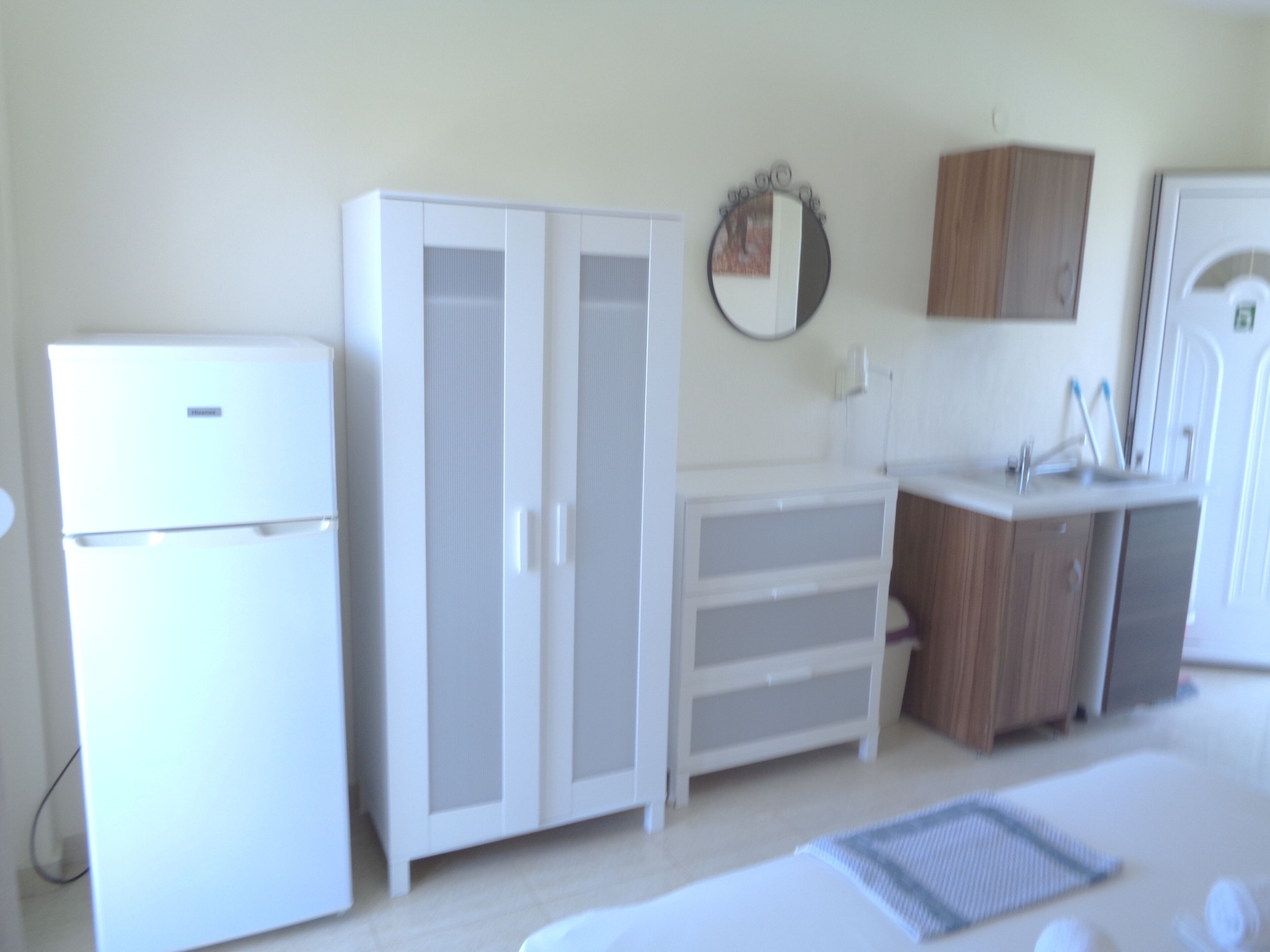 Una cocina moderna con armarios blancos, un refrigerador, un lavamanos y un espejo sobre la encimera.