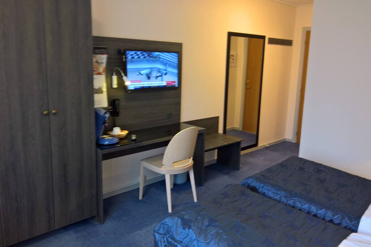 A hotel room with a desk, chair, and a bed.