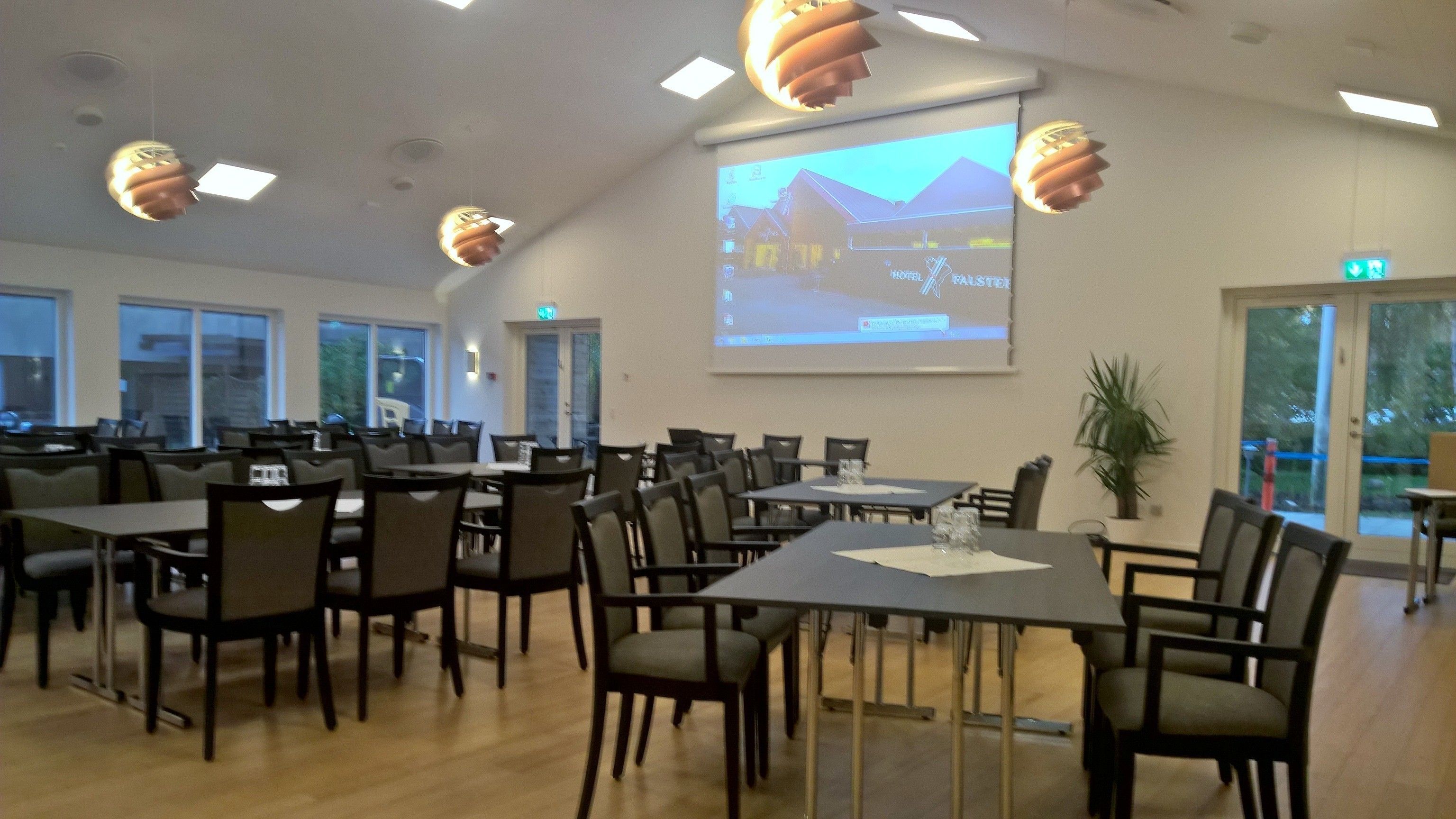 A conference room with tables and chairs, a projector screen displaying a landscape, and a potted plant.