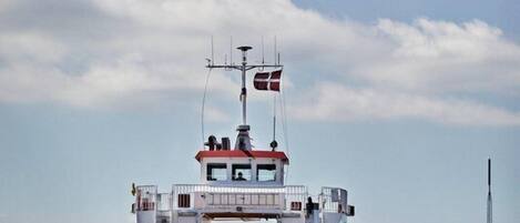 A ferry with a cabin and a deck, moving on water with a clear sky in the background.
