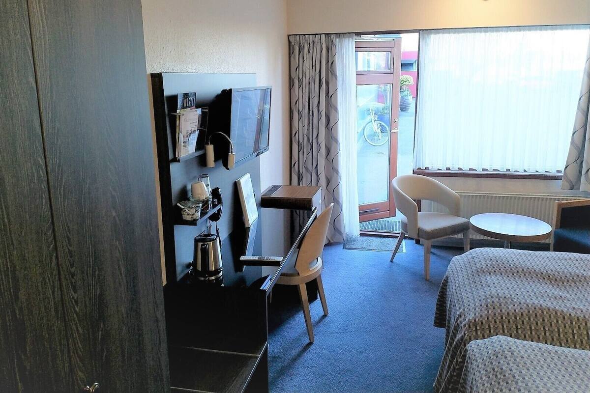 A hotel room with a bed, a desk with a chair, a television, and a window with curtains.