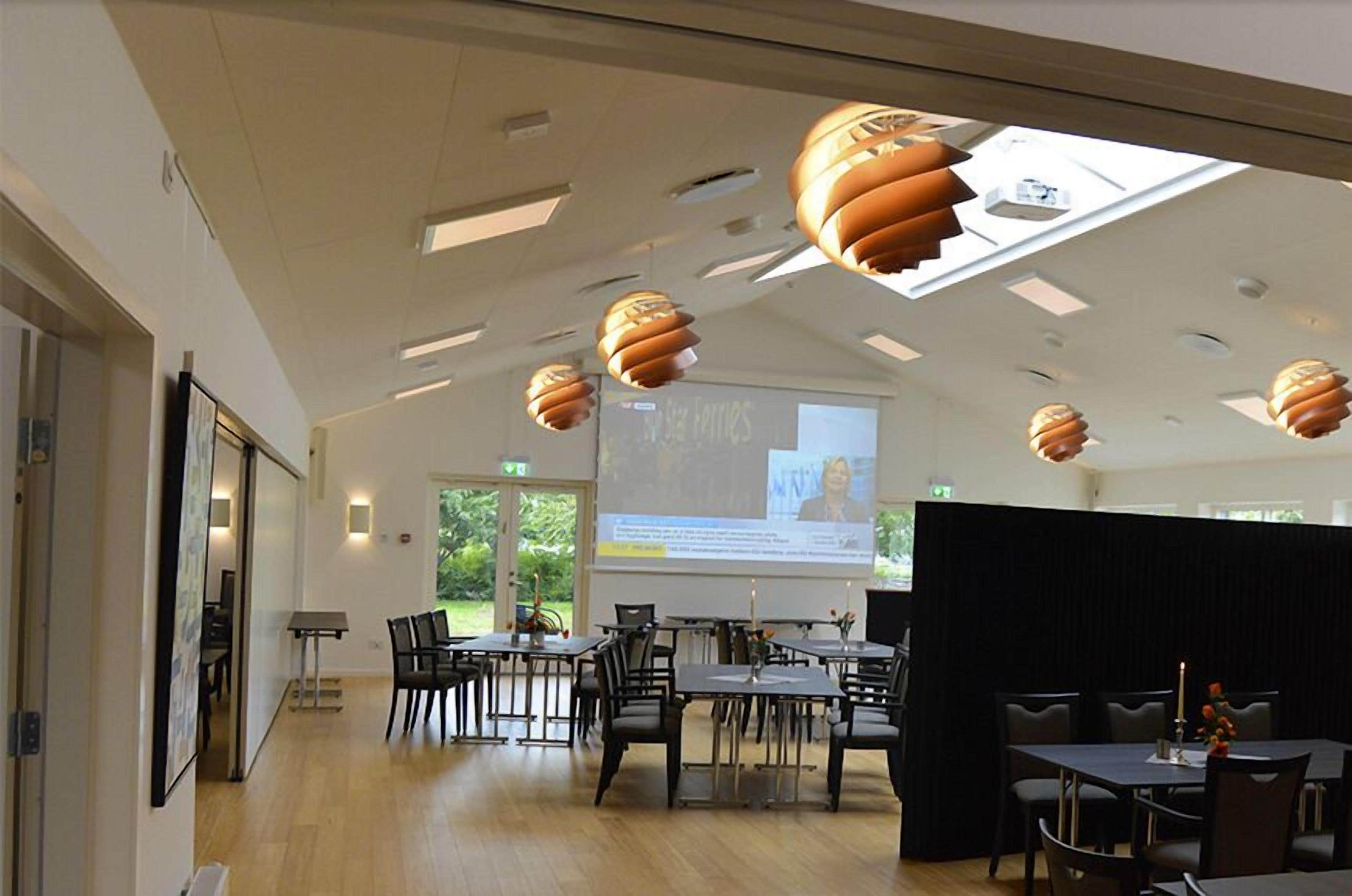 A conference room with tables, chairs, a projector screen, and a large window.