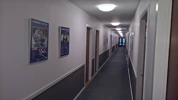 Un long couloir étroit, avec des portes de chaque côté, des affiches sur les murs et un sol recouvert de moquette.
