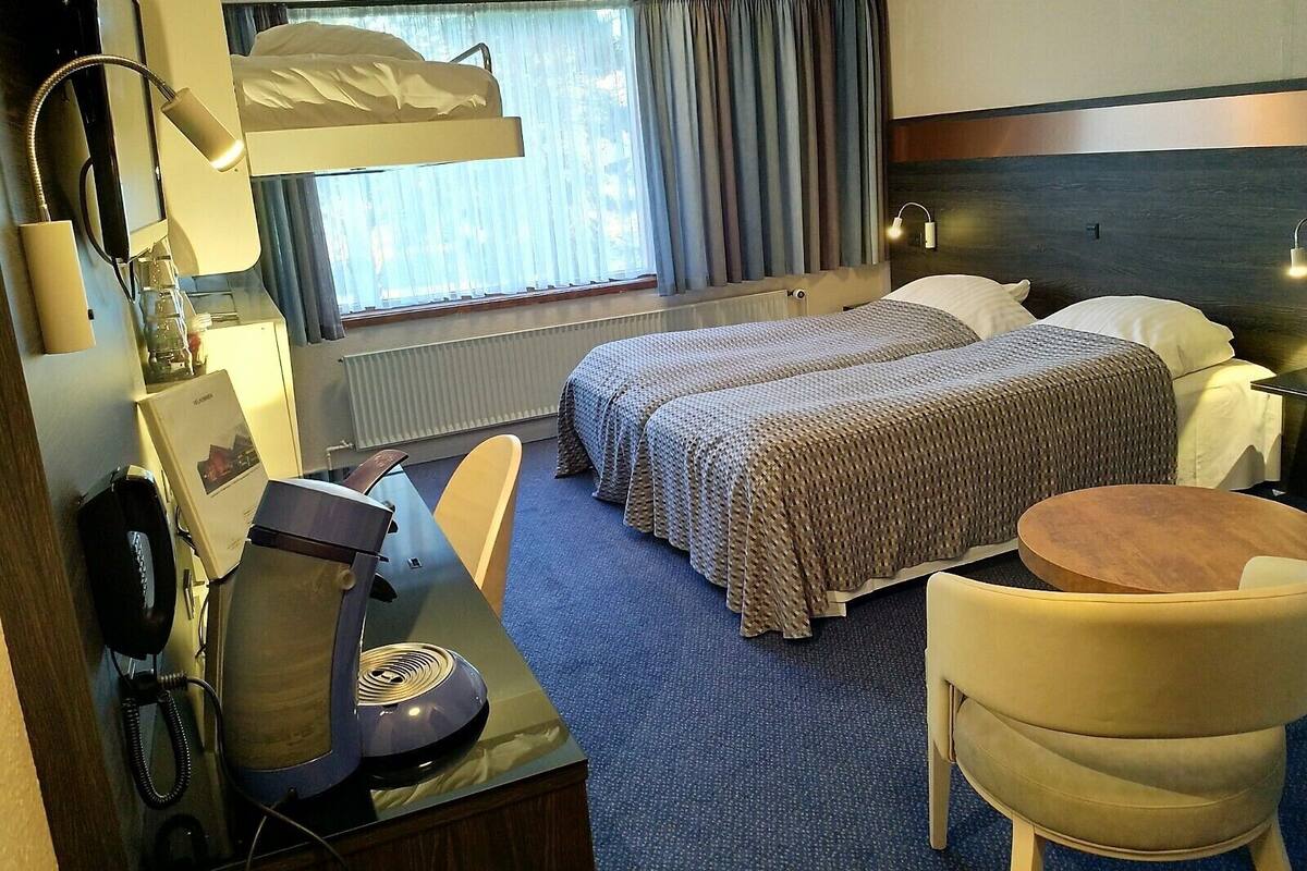 A hotel room with a bed, two bedside tables, a desk with a chair, a lamp, and a telephone.