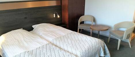A hotel room with two beds, a wooden headboard, a small table, two chairs, and a wall-mounted light.