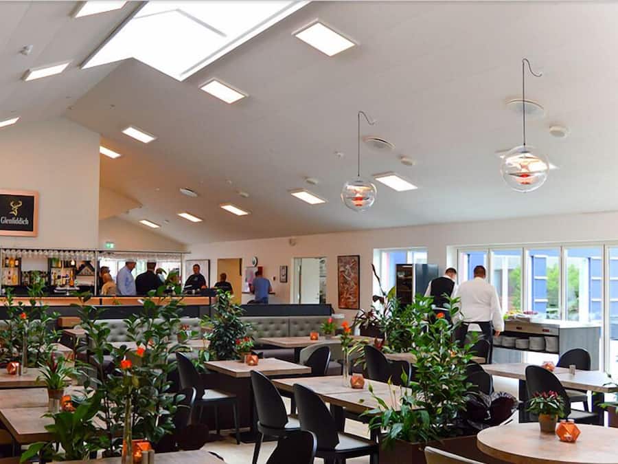 A restaurant with a bar area, multiple tables and chairs, and large windows allowing natural light.