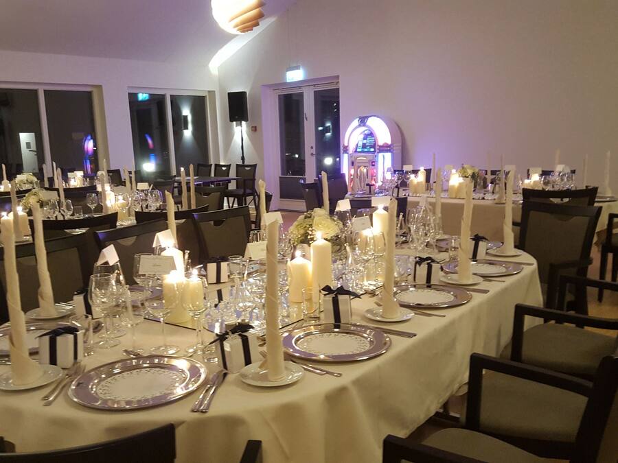A banquet hall with tables set for a formal event, featuring white tablecloths, candles, and silverware.