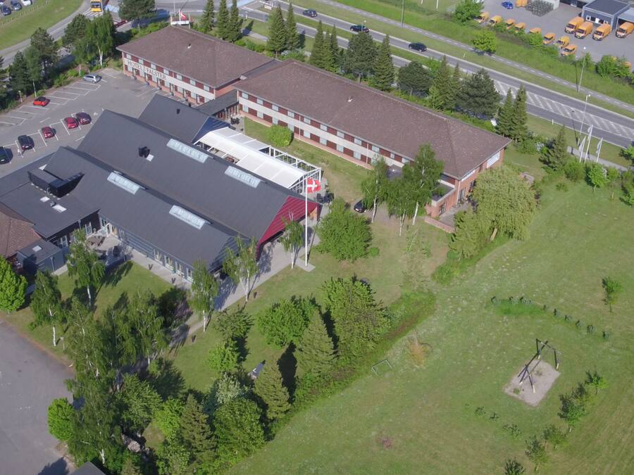 An aerial view of a hotel with a parking lot, a green lawn, and a road with vehicles.
