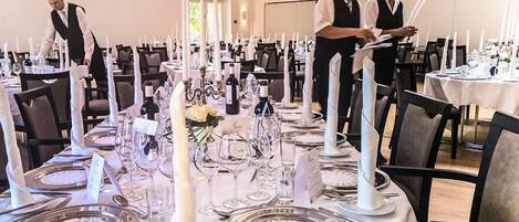 Comedor formal con mesas dispuestas para varios comensales, cada una con cubiertos, platos y copas.