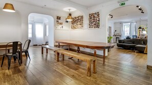 A spacious room with a long wooden table, benches, and a black leather sofa. - Hostel Casa d'Alagoa (Faro)