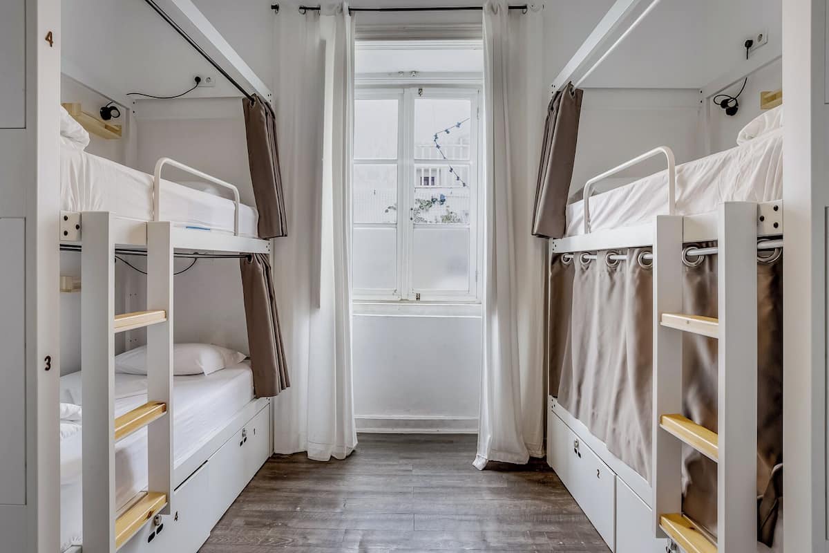 A dormitory room with bunk beds, a window, and curtains.
