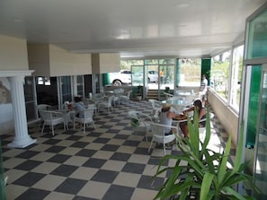 Una cafetería con suelo a cuadros, sillas blancas y ventanas amplias.