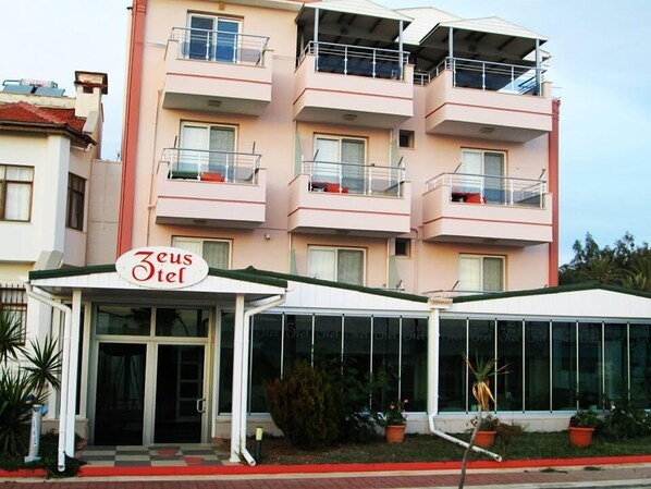Un hotel de varios pisos llamado Zeus Hotel, con balcones y una entrada cubierta.
