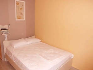 A single bed with white bedding in a room with a peach-colored wall and a small bedside table with a lamp. - Zeus Hotel (Silifke)