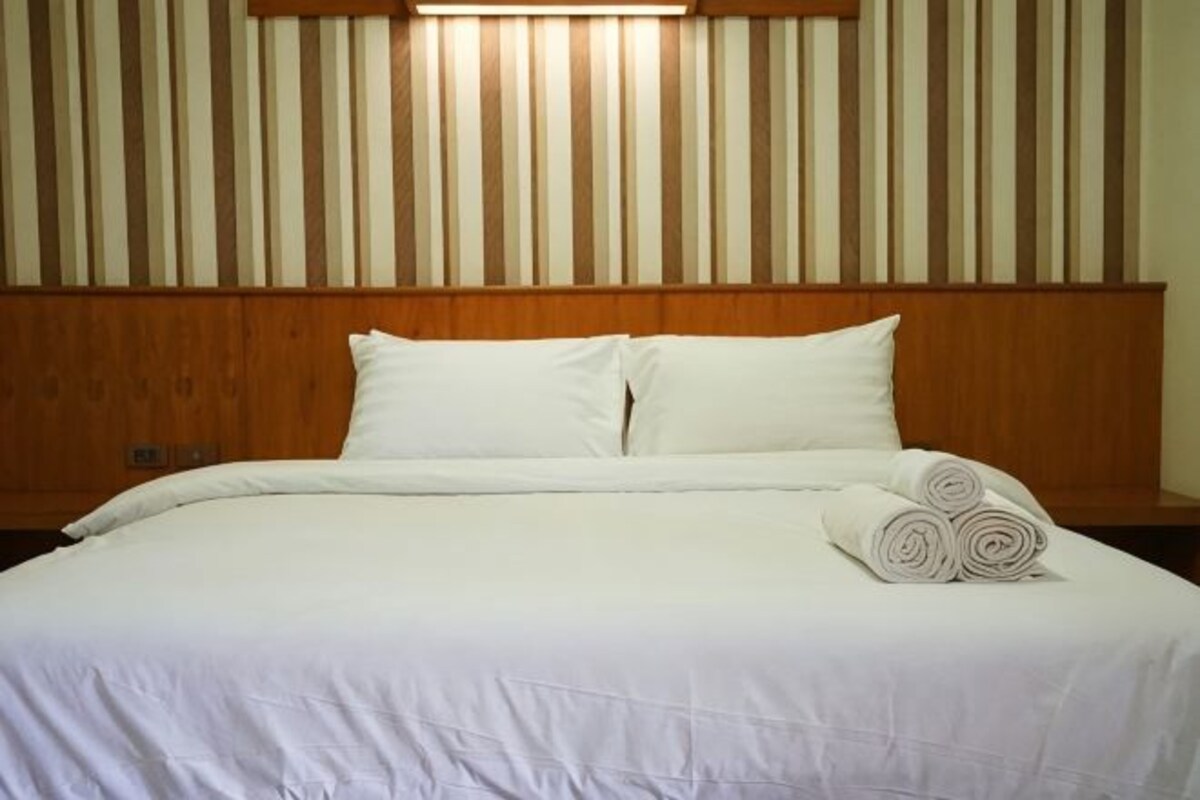 Un lit bien fait, avec du linge de lit blanc et des oreillers, une tête de lit en bois et un mur recouvert de lattes de bois verticales.