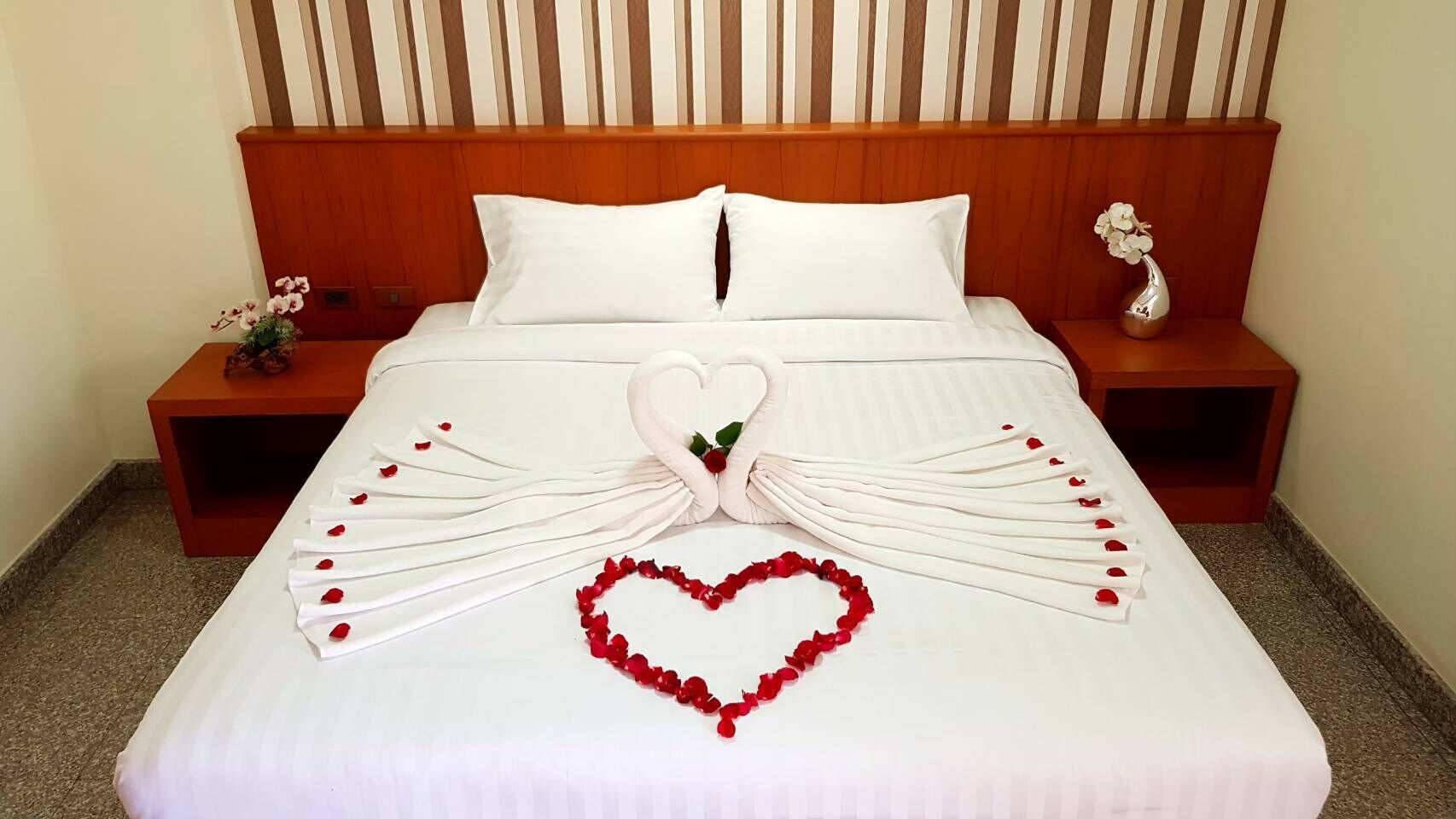 Una cama bien arreglada con un arreglo floral con forma de corazón y un diseño de cisne en la colcha.