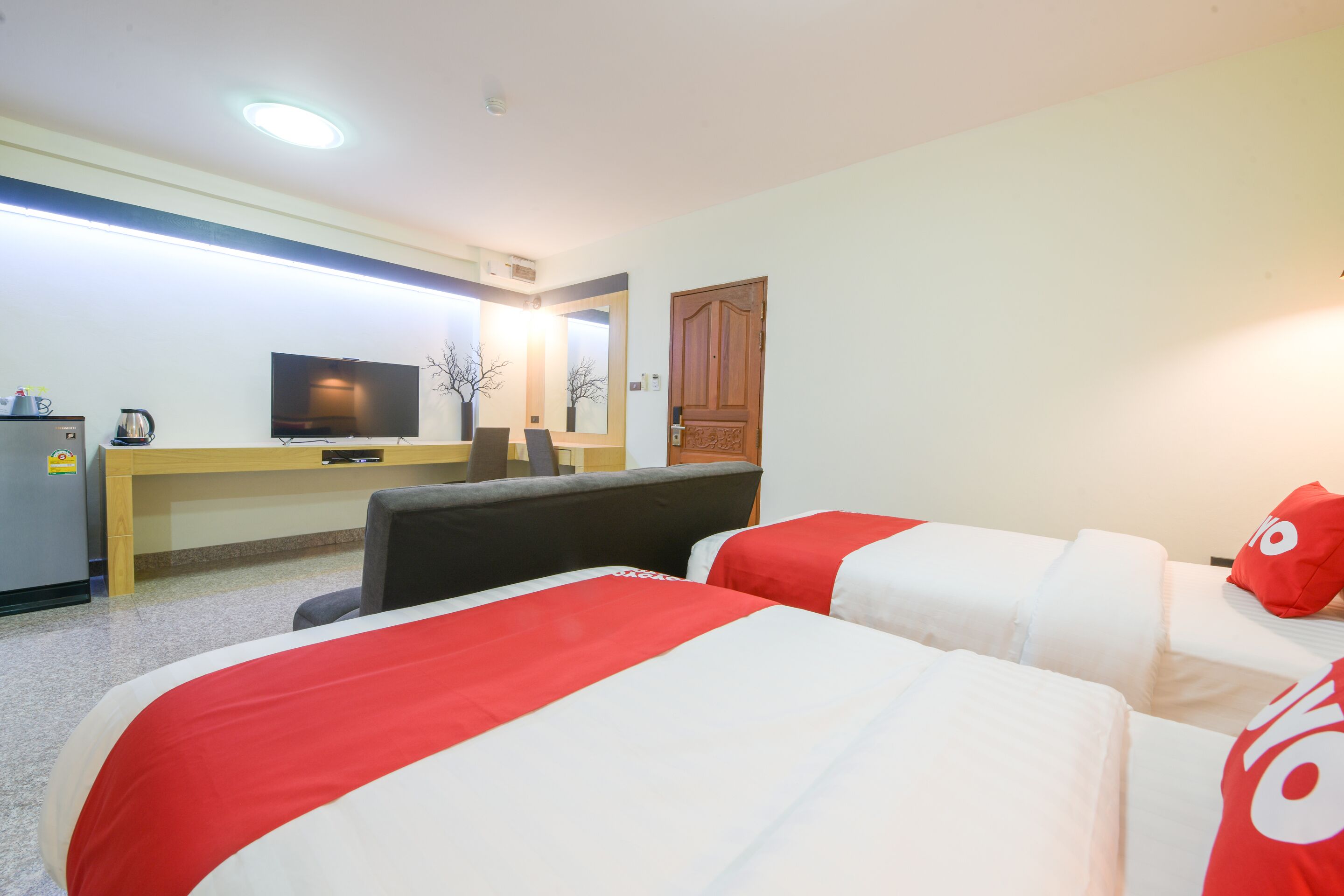 A hotel room with two beds, a desk, a television, and a door.