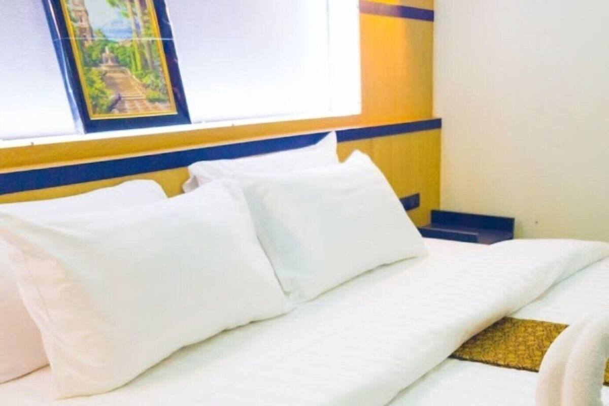 A neatly made bed with white linens, a window with a view of a building, and a towel on the bed.