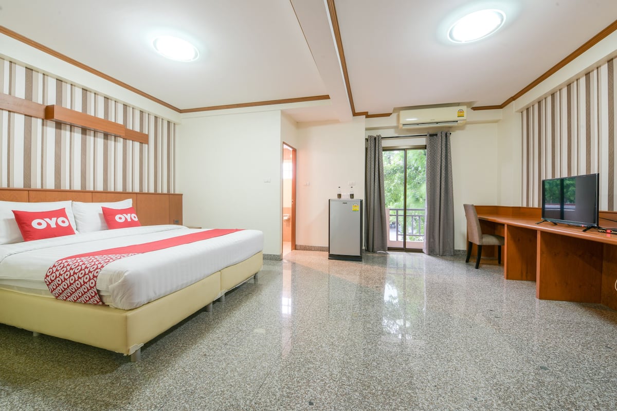 A hotel room with a bed, desk, TV, and an air conditioning unit.