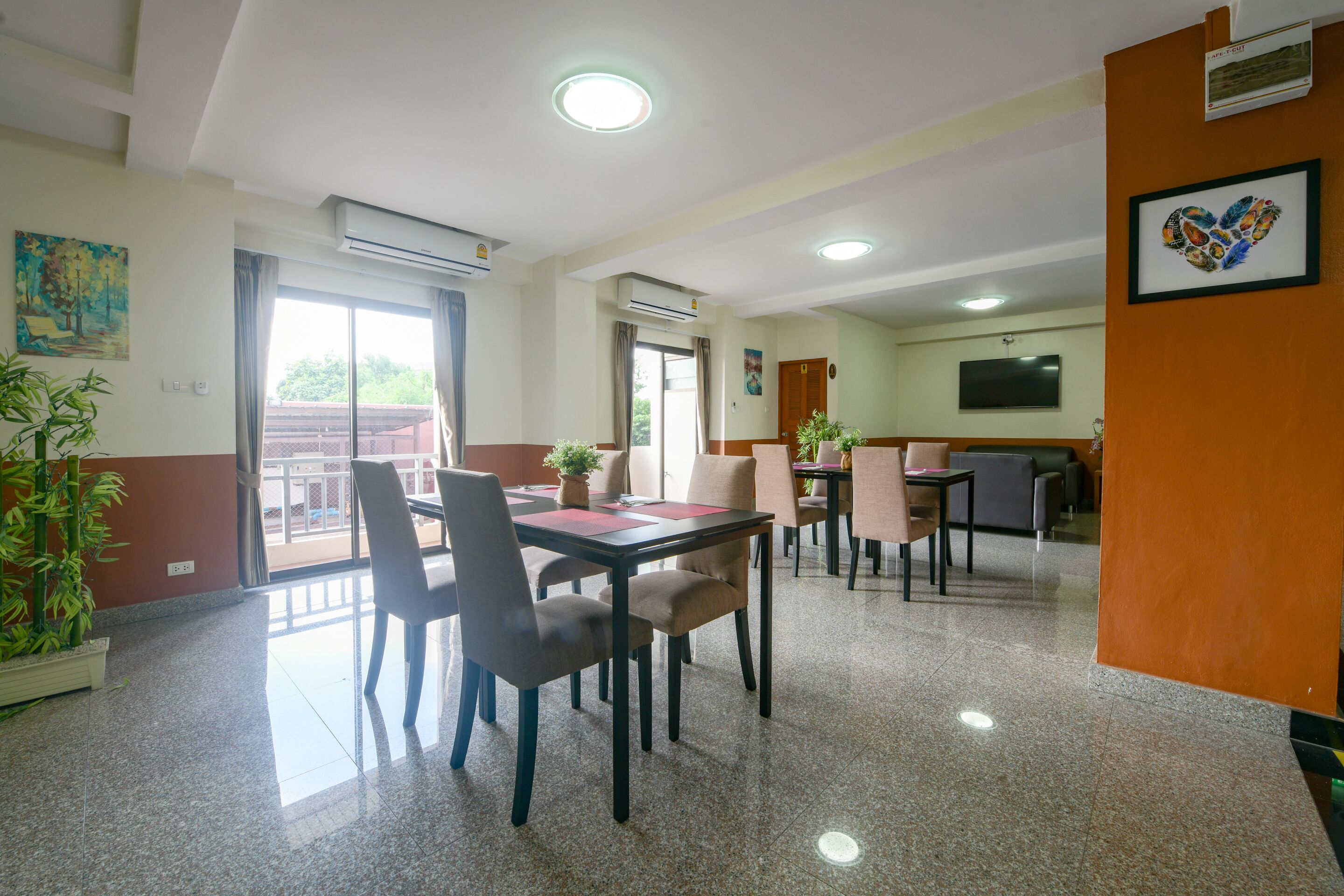 A spacious dining area with a large table and chairs, a television mounted on the wall, and a balcony with a view.